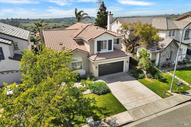mediterranean / spanish house with a tile roof, a chimney, driveway, a garage, and stucco siding