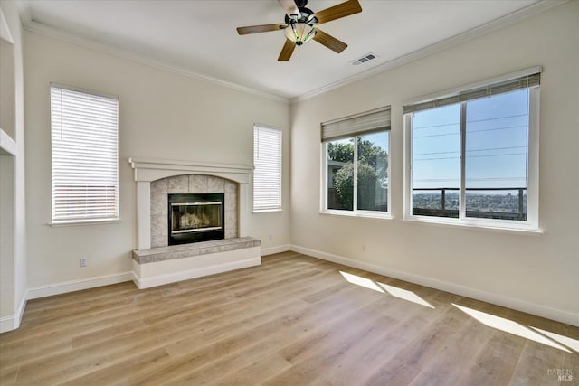 unfurnished living room featuring light wood-type flooring, a tile fireplace, baseboards, ornamental molding, and visible vents