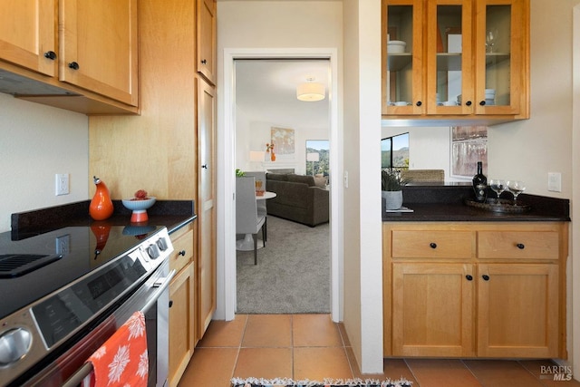 kitchen featuring dark countertops, light tile patterned floors, stainless steel electric stove, glass insert cabinets, and light colored carpet