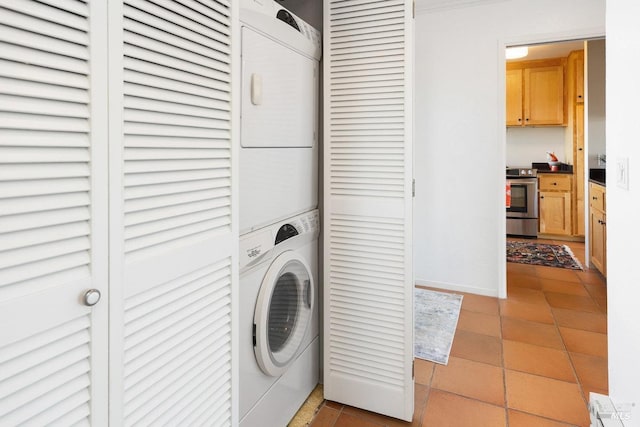 laundry area with stacked washer / drying machine, baseboards, light tile patterned floors, and laundry area