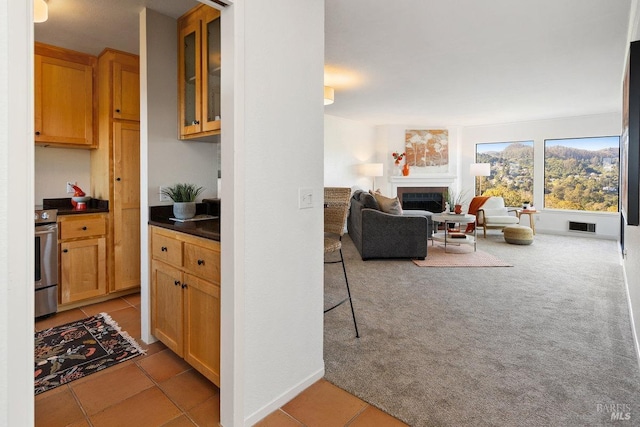 kitchen featuring electric stove, visible vents, light colored carpet, a fireplace, and open floor plan
