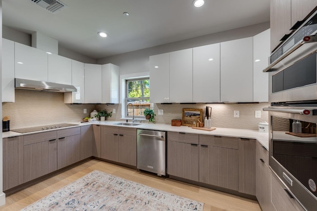kitchen featuring under cabinet range hood, visible vents, a sink, light wood-type flooring, and appliances with stainless steel finishes