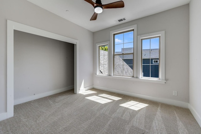 empty room with carpet floors, visible vents, a wealth of natural light, and a ceiling fan