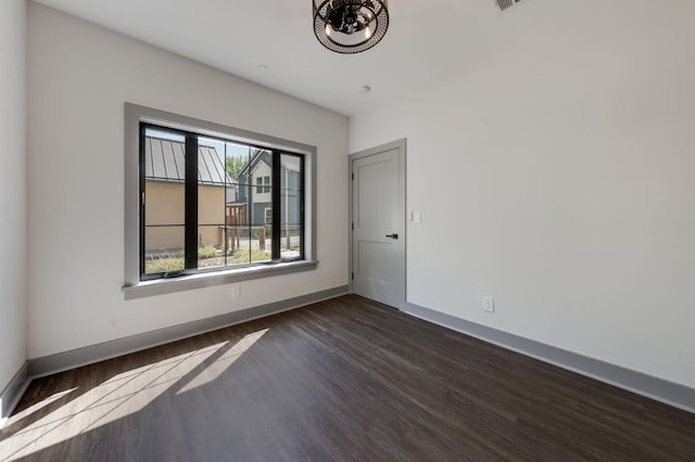 empty room featuring baseboards, dark wood-style floors, and an inviting chandelier