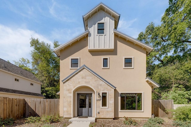 rear view of house with stucco siding, fence, stone siding, and board and batten siding