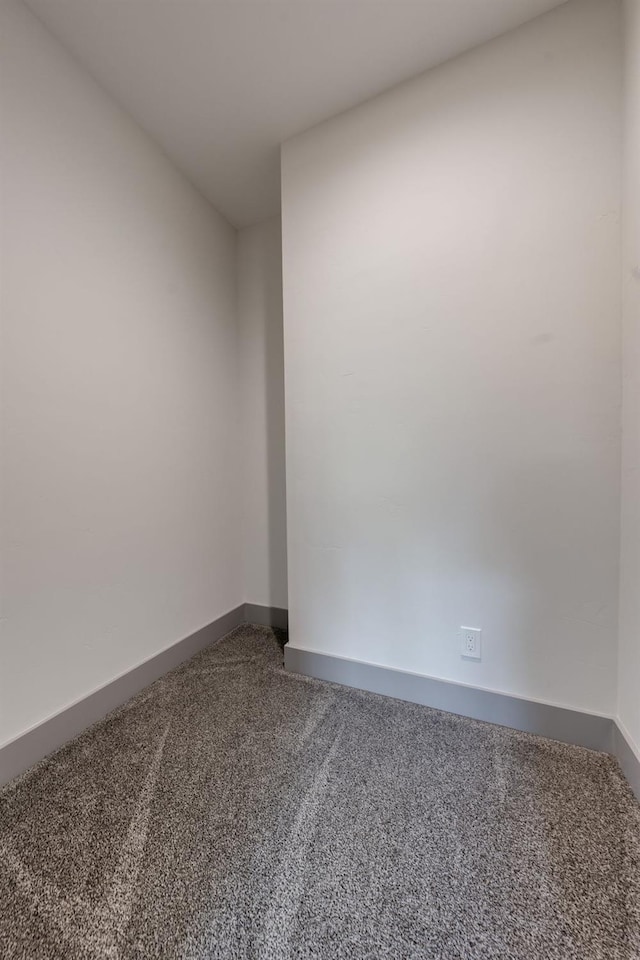 spare room with baseboards and dark carpet