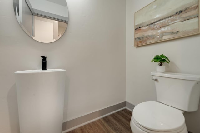 half bath with baseboards, wood finished floors, and toilet