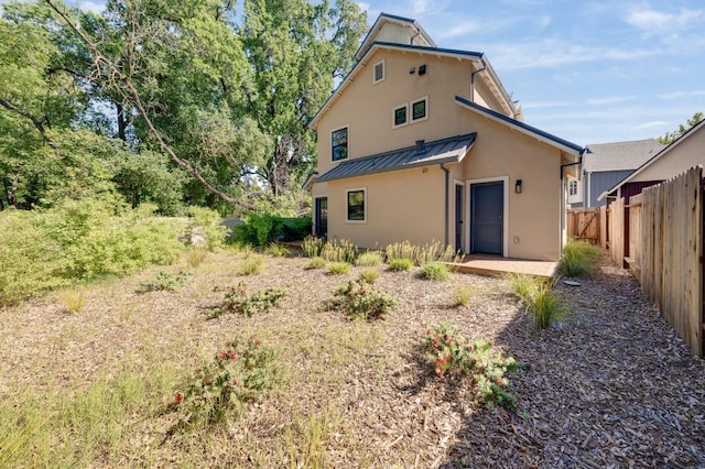 rear view of property featuring fence, a standing seam roof, metal roof, and stucco siding