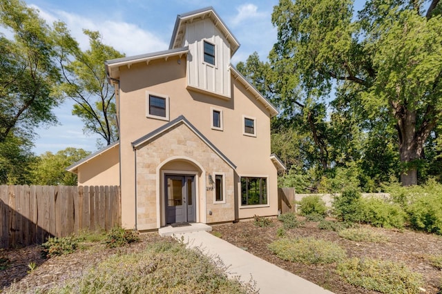 view of front of house with stucco siding, stone siding, and fence