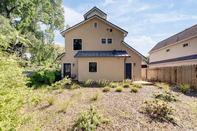 rear view of house with stucco siding, metal roof, a standing seam roof, and fence