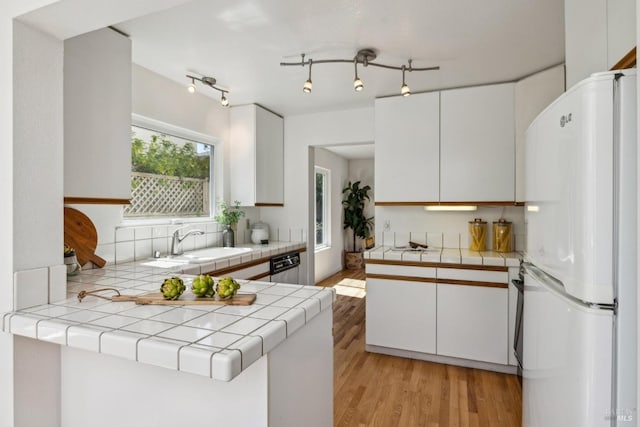 kitchen featuring white cabinets, tile countertops, a sink, freestanding refrigerator, and light wood-style floors
