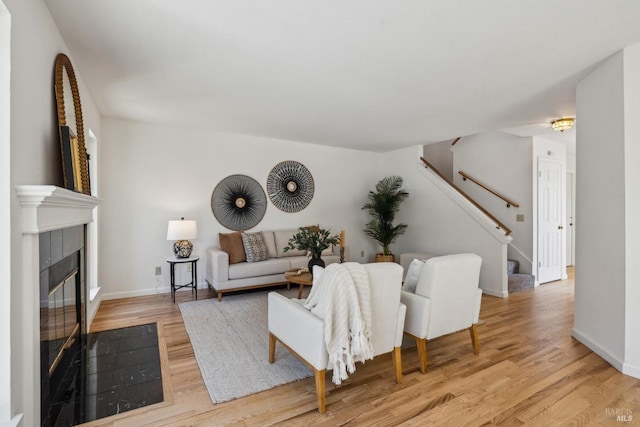 living room with a tile fireplace, baseboards, stairs, and light wood-style flooring