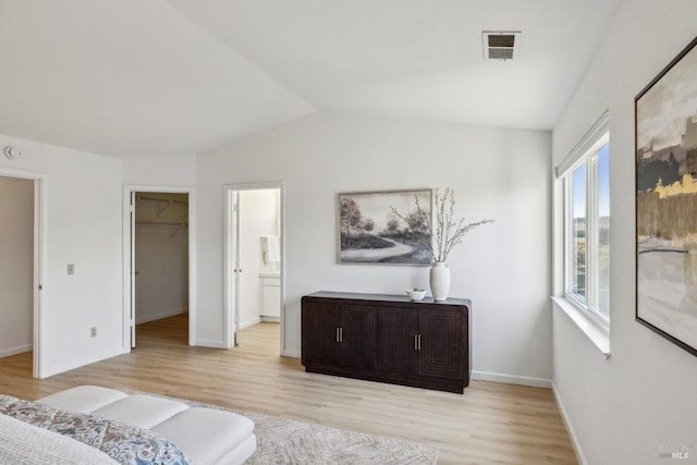 bedroom with light wood-type flooring, vaulted ceiling, baseboards, visible vents, and a walk in closet