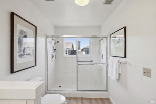 bathroom with toilet, wood finished floors, visible vents, and a stall shower