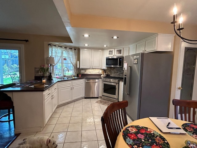 kitchen with a sink, light tile patterned floors, stainless steel appliances, a peninsula, and white cabinetry