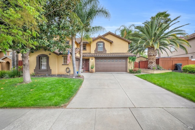 mediterranean / spanish house with stucco siding, fence, driveway, a front lawn, and an attached garage