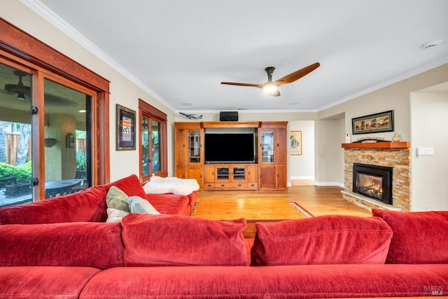 living area with wood finished floors, ceiling fan, a stone fireplace, and crown molding