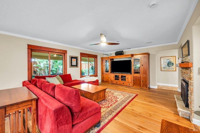 living room featuring crown molding, ceiling fan, a stone fireplace, and light wood-style flooring