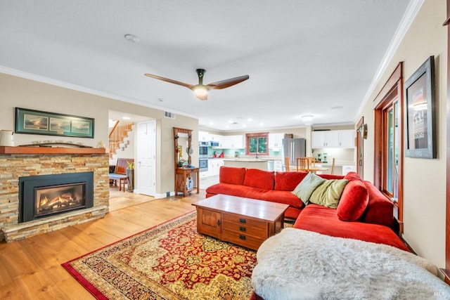 living room featuring light wood finished floors, stairway, visible vents, a stone fireplace, and ornamental molding