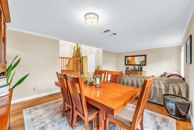 dining space with baseboards, visible vents, ornamental molding, and wood finished floors