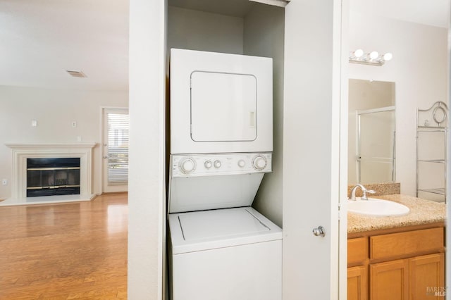 clothes washing area with a sink, light wood-style floors, stacked washing maching and dryer, visible vents, and laundry area