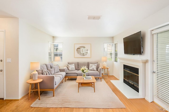 living room with wood-type flooring, a glass covered fireplace, plenty of natural light, and visible vents