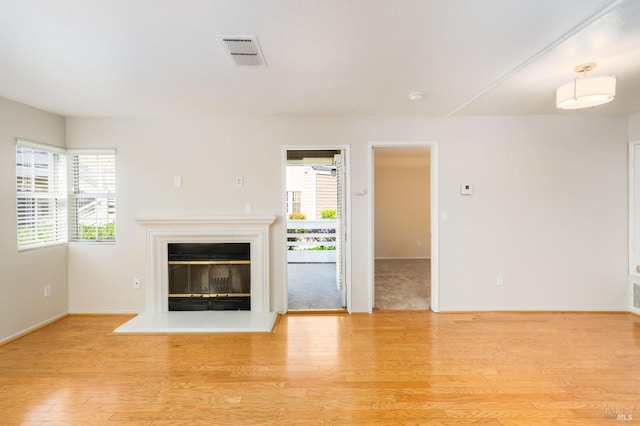 unfurnished living room with a glass covered fireplace, light wood-style flooring, visible vents, and a healthy amount of sunlight
