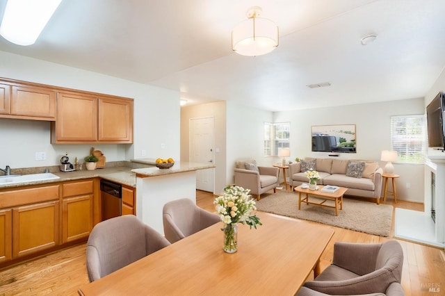 kitchen featuring light wood finished floors, a sink, open floor plan, dishwasher, and light countertops