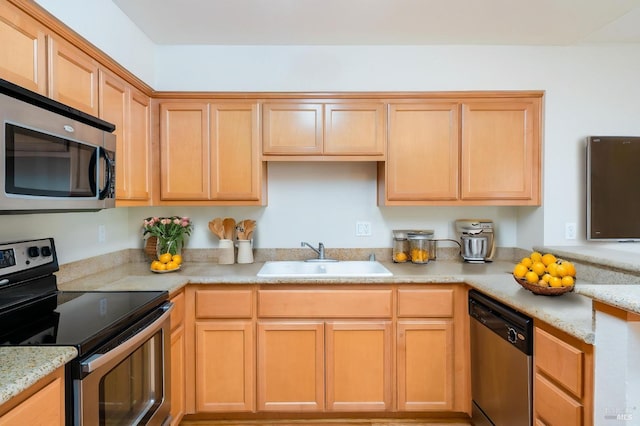 kitchen featuring light brown cabinets, light stone counters, stainless steel appliances, and a sink