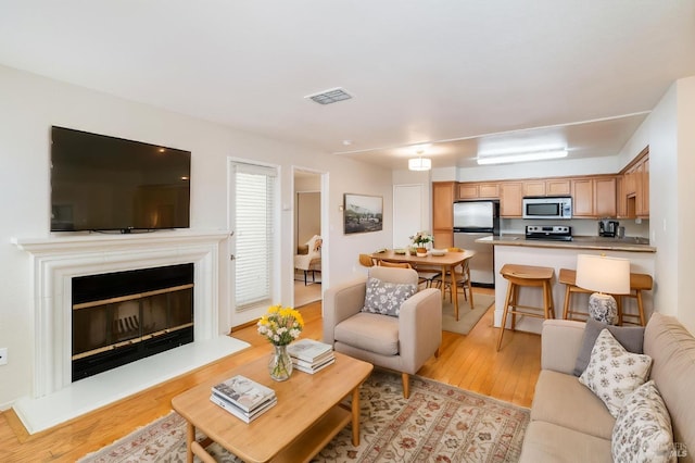 living room with a glass covered fireplace, light wood-style flooring, and visible vents