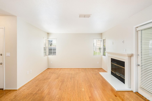 unfurnished living room with light wood finished floors, a glass covered fireplace, a wealth of natural light, and visible vents