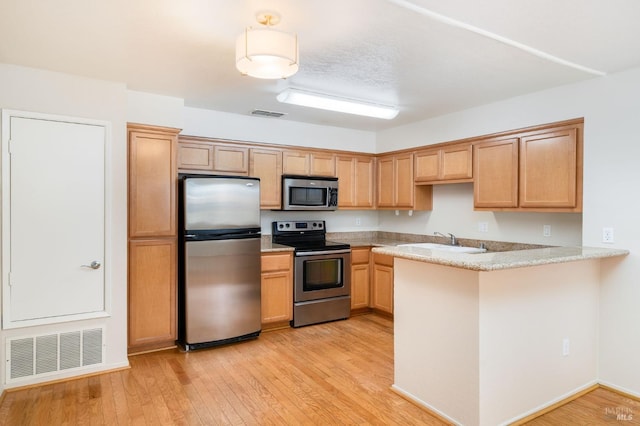 kitchen featuring stainless steel appliances, light wood finished floors, light countertops, a peninsula, and visible vents
