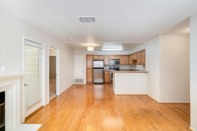 kitchen with a peninsula, stainless steel appliances, visible vents, and light wood-style floors
