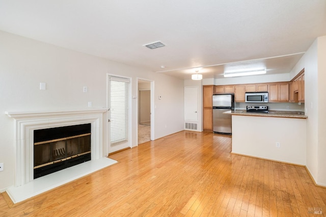 kitchen with a glass covered fireplace, stainless steel appliances, visible vents, and light wood-style floors