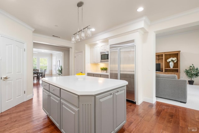 kitchen with gray cabinets, visible vents, built in appliances, crown molding, and wood-type flooring
