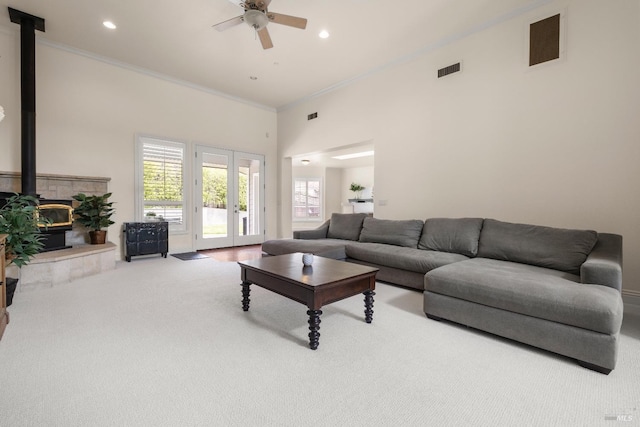 carpeted living area with ceiling fan, ornamental molding, a wood stove, and visible vents