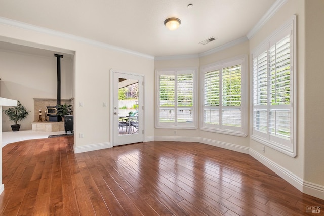 spare room featuring baseboards, a wood stove, hardwood / wood-style floors, and visible vents