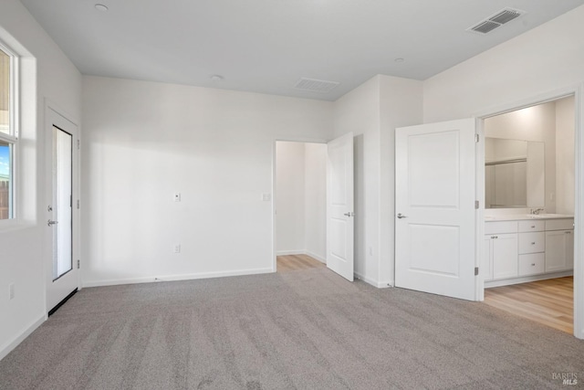 unfurnished bedroom with light carpet, a sink, baseboards, visible vents, and connected bathroom