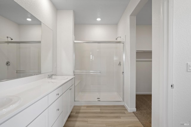 bathroom with wood finished floors, a sink, double vanity, and a stall shower
