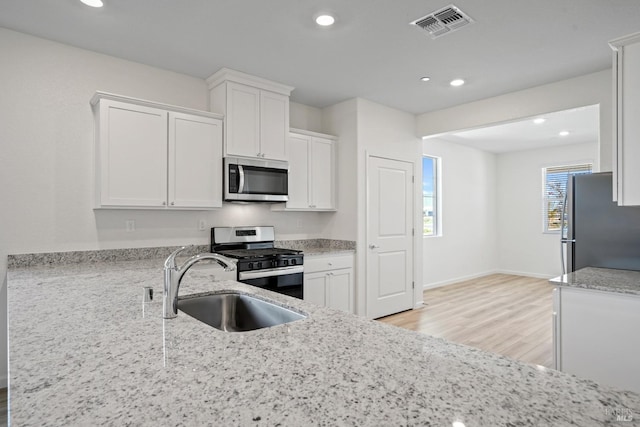 kitchen featuring light wood finished floors, stainless steel appliances, white cabinets, a sink, and visible vents