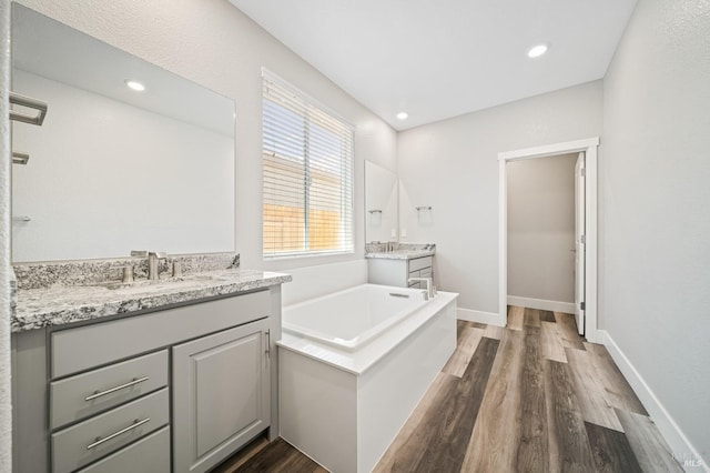 full bath with two vanities, a sink, baseboards, wood finished floors, and a garden tub