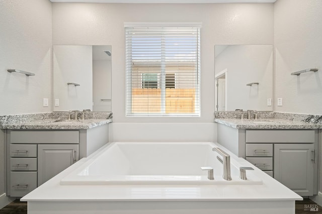 full bath with a bath, a sink, and two vanities