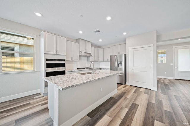 kitchen with a sink, stainless steel appliances, baseboards, under cabinet range hood, and visible vents