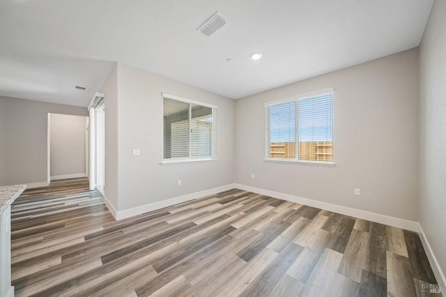 empty room with wood finished floors, visible vents, and baseboards