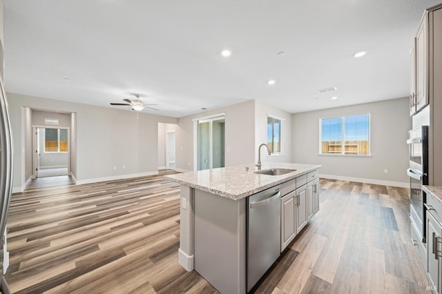 kitchen with light wood finished floors, stainless steel appliances, a sink, baseboards, and a kitchen island with sink