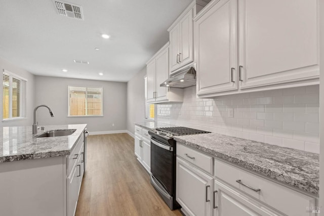 kitchen featuring white cabinets, under cabinet range hood, a sink, gas range oven, and light wood-style flooring