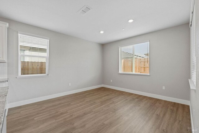 unfurnished room featuring baseboards, light wood finished floors, and plenty of natural light