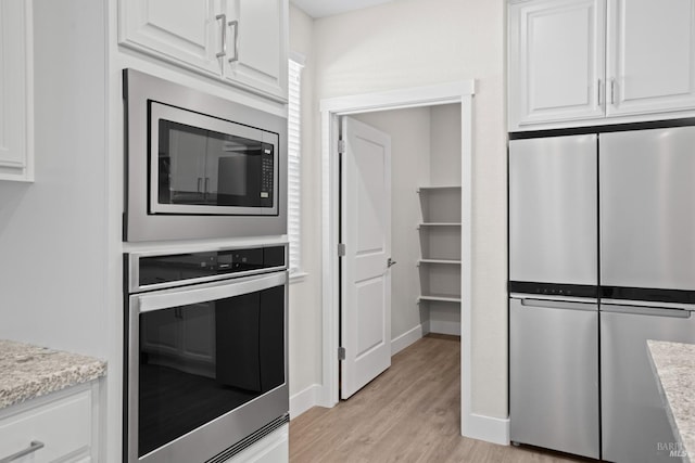 kitchen with light wood finished floors, white cabinets, baseboards, light stone countertops, and appliances with stainless steel finishes