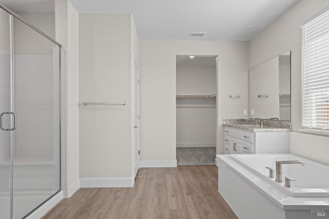 bathroom featuring a spacious closet, wood finished floors, visible vents, a bath, and a stall shower
