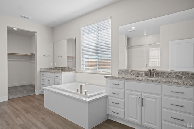 full bathroom with a garden tub, two vanities, wood finished floors, and a sink